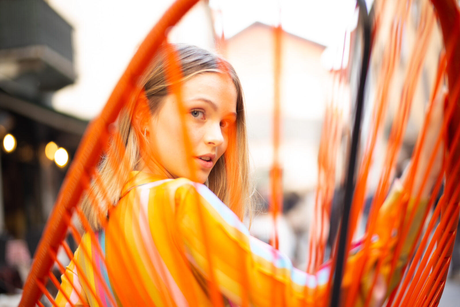 Woman looking back over her shoulder through the orange cords of a patio chair
