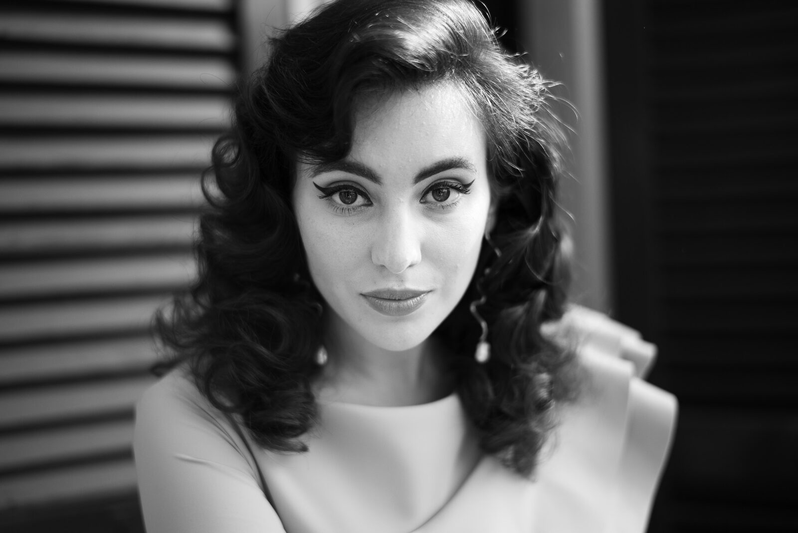 Black and white portrait of a woman with vintage curls in front of window shutters