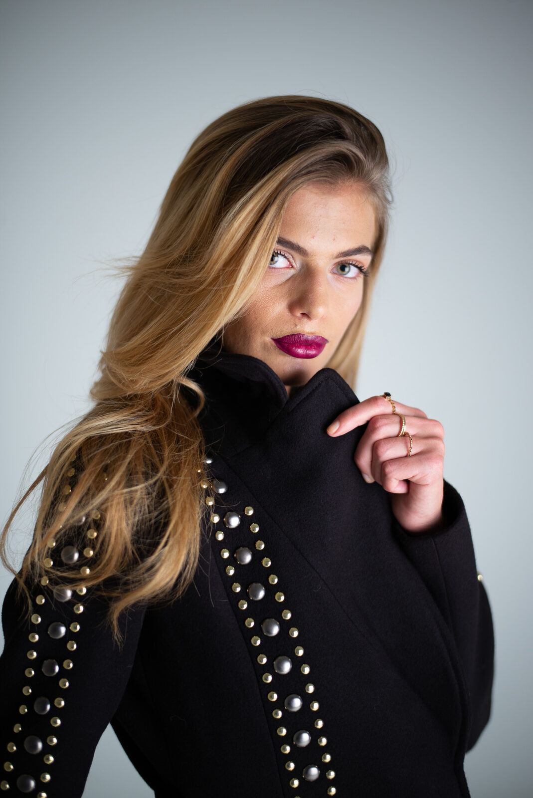 Studio portrait of a woman in a studded black coat with deep berry lipstick